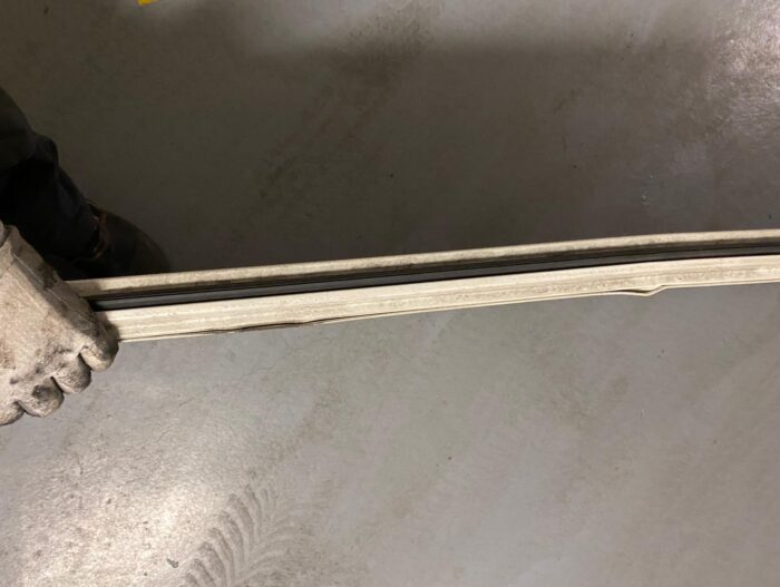 WhatsApp Image 2024-07-28 at 14.35.46 Ręka w rękawiczce ściska długi, prostokątny metalowy pasek z widoczną ciemną linią biegnącą przez środek, umieszczony na teksturowanym szarym tle – przedstawiony na warszawskiej stronie internetowej poświęconej naprawie bram, rolet i barier.