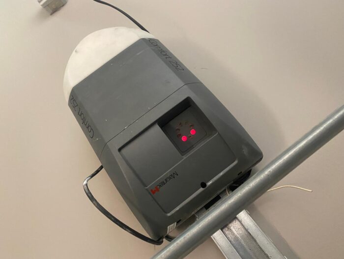 WhatsApp Image 2024-07-28 at 18.22.12 Na stronie internetowej znajduje się obraz przedstawiający kontroler Linear Xtreme Controller 252 bezpiecznie zamontowany na szarej ścianie, z dwoma świecącymi na czerwono lampkami kontrolnymi oznaczającymi jego stan operacyjny. Pod kontrolerem wyraźnie widoczna jest metalowa szyna, która podkreśla elementy zwykle używane do napraw bram, rolet i barier w Warszawie.