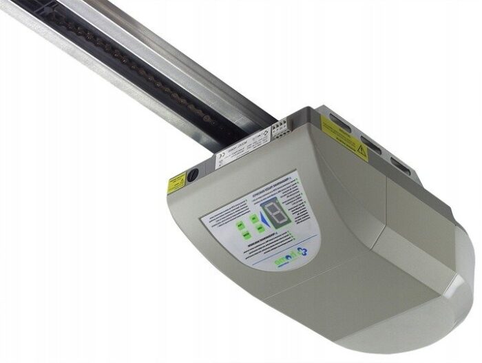 pol_pl_NAPED-DO-BRAMY-GARAZOWEJ-CAME-HOME-HG1000-286_2 Obraz na stronie internetowej przedstawia biały automatyczny otwieracz drzwi garażowych zainstalowany na suficie. Urządzenie to obejmuje cyfrowy panel wyświetlacza i wiele przycisków operacyjnych, z solidną metalową szyną rozciągającą się na zewnątrz, wszystko zaprojektowane do wydajnego sterowania i przesuwania bram, rolet i barier w Warszawie.