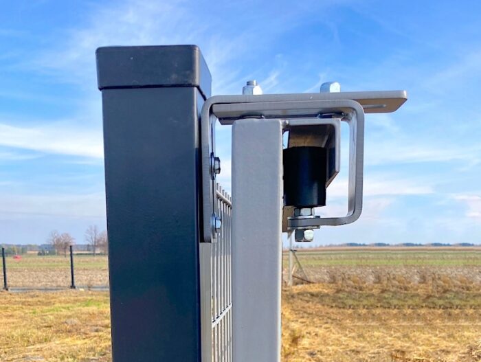 06776db64dc5995d3b463c7c2a34 Obraz na stronie internetowej przedstawia szczegółowy widok solidnej metalowej bramy wyposażonej w najnowocześniejszy mechanizm blokujący. Umieszczona w wiejskim otoczeniu, ta brama jest bezpiecznie zamontowana na mocnym czarnym słupku. W tle znajduje się rozległe otwarte pole pod czystym, błękitnym niebem, podkreślające funkcjonalną i bezpieczną konstrukcję bramy w harmonii z jej naturalnym otoczeniem.