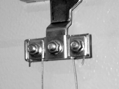 118_1 Na zdjęciu zamieszczonym na stronie internetowej poświęconej naprawie bram, rolet i barier w Warszawie czarno-białe zdjęcie przedstawia metalowy uchwyt przymocowany do ściany. Uchwyt charakteryzuje się prostą, przemysłową estetyką. Do jego spodniej strony przymocowane są dwa cienkie druty, każdy zabezpieczony śrubą.