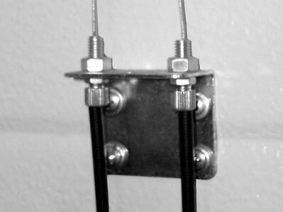 119_2 Obraz na stronie internetowej przedstawia czarno-białe zbliżenie dwóch kabli przymocowanych do metalowej płyty montażowej przymocowanej do ściany. Płyta jest solidnie przymocowana śrubami na każdym rogu, a kable są wyposażone w metalowe okucia na górnych końcach.