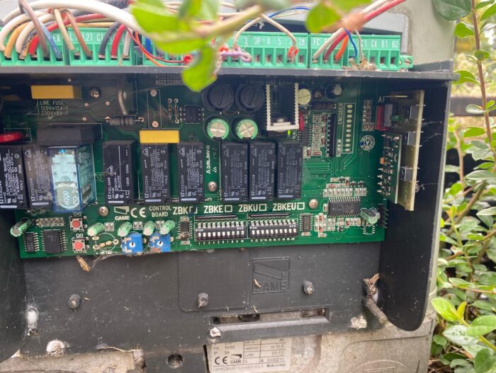 WhatsApp Image 2024-08-04 at 15.34.06 Obraz na naszej stronie internetowej przedstawia szczegółowy widok płytki drukowanej umieszczonej w zewnętrznej skrzynce elektrycznej. Ta skomplikowana konstrukcja obejmuje kilka przekaźników, kondensatorów i szereg przewodów, którym towarzyszy bezpiecznik umieszczony po lewej stronie. Cały zespół jest osadzony pośród bujnej zieleni, co podkreśla jego zewnętrzną lokalizację w Warszawie.