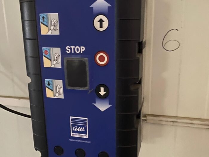 WhatsApp Image 2024-08-10 at 16.29.26 Obraz na stronie internetowej przedstawia niebieski panel sterowania przeznaczony do obsługi bram, rolet i barier. Panel jest eksponowany w widocznym miejscu i zawiera wyraźnie oznaczone przyciski odpowiadające funkcjom „w górę”, „w dół” i „stop”. Obok tych przycisków znajdują się etykiety diagramów z instrukcjami użytkownika dotyczącymi bezproblemowej obsługi. Logo firmy jest elegancko umieszczone na dole panelu, zapewniając widoczność marki. Ponadto obok panelu sterowania na ścianie znajduje się pogrubiona liczba „6”, prawdopodobnie wskazująca na odniesienie do instalacji lub identyfikator sprzętu.