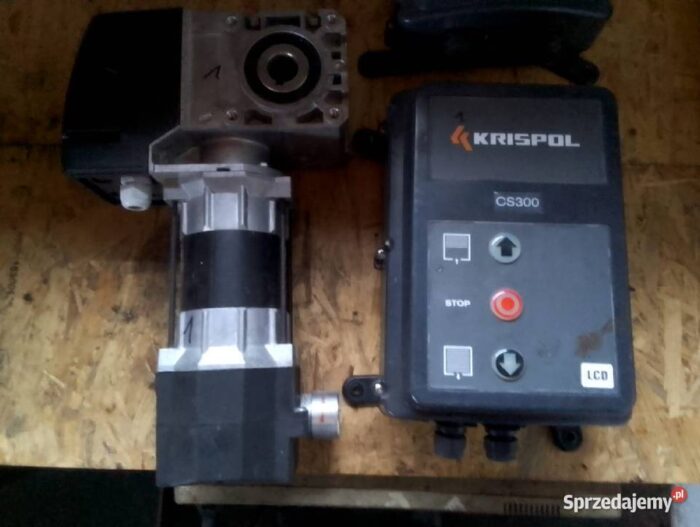 sterownik-bramy-garazowej-krispol-podlaskie-uslugi-budowlane-574883565 Na stronie internetowej znajduje się szczegółowy obraz jednostki sterującej KRISPOL CS300, idealnie dostosowanej do platformy skupionej na naprawie bram, rolet i barier w Warszawie. To zbliżenie pokazuje jednostkę sterującą umieszczoną na drewnianej powierzchni, podkreślając jej opisane przyciski, takie jak „STOP” i strzałki kierunkowe. Wyświetlacz LCD jest zintegrowany z projektem, aby zapewnić wyraźną widoczność ustawień. Metalowy silnik ma strukturę kątową i jest bezpiecznie przymocowany do jednostki sterującej, podkreślając funkcjonalną inżynierię tego sprzętu.