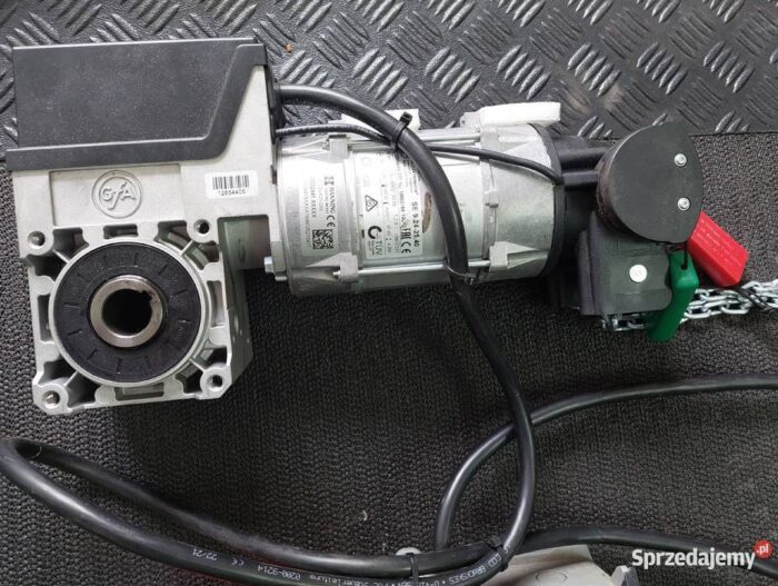 zestaw-centrala-sterujaca-naped-gfa-do-bramy-ogrodzenia-bramy-slaskie-chorzow-559724107 Na zdjęciu wyraźnie widać zbliżenie silnika elektrycznego wyposażonego w przymocowaną skrzynię biegów, któremu towarzyszą czarne przewody zasilające i łańcuch bezpieczeństwa dla dodatkowego bezpieczeństwa. Silnik jest umieszczony na metalicznym tle charakteryzującym się charakterystycznym wzorem diamentowym. Na powierzchni silnika wyraźnie widać kilka etykiet i ostrzeżeń, podkreślających bezpieczeństwo i instrukcje obsługi. To szczegółowe przedstawienie można znaleźć na stronie internetowej specjalizującej się w naprawie bram, rolet i barier w Warszawie.