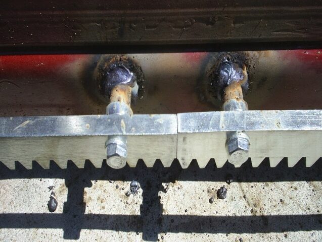 M4034S-4211 Na zdjęciu widać szczegółowo dwa spawane metalowe połączenia na powierzchni, którym towarzyszą widoczne śruby i metalowy wspornik. Spoiny wykazują niewielkie odbarwienia, co sugeruje narażenie na działanie ciepła, a ciemne plamy są rozrzucone po okolicy. Ta ilustracja przedstawia rodzaj prac naprawczych podejmowanych w przypadku bram, rolet i barier w Warszawie.